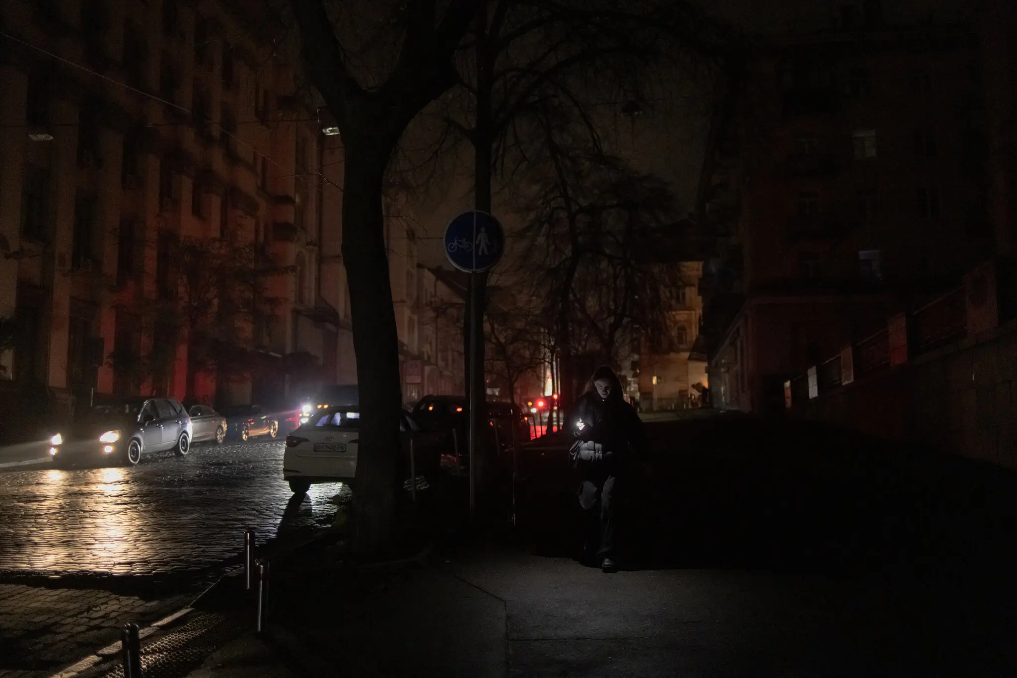 Темна вулиця під час часткового відключення світла в листопаді в Києві, де мешканці покладаються на ліхтарики мобільних телефонів, щоб орієнтуватися в темряві.